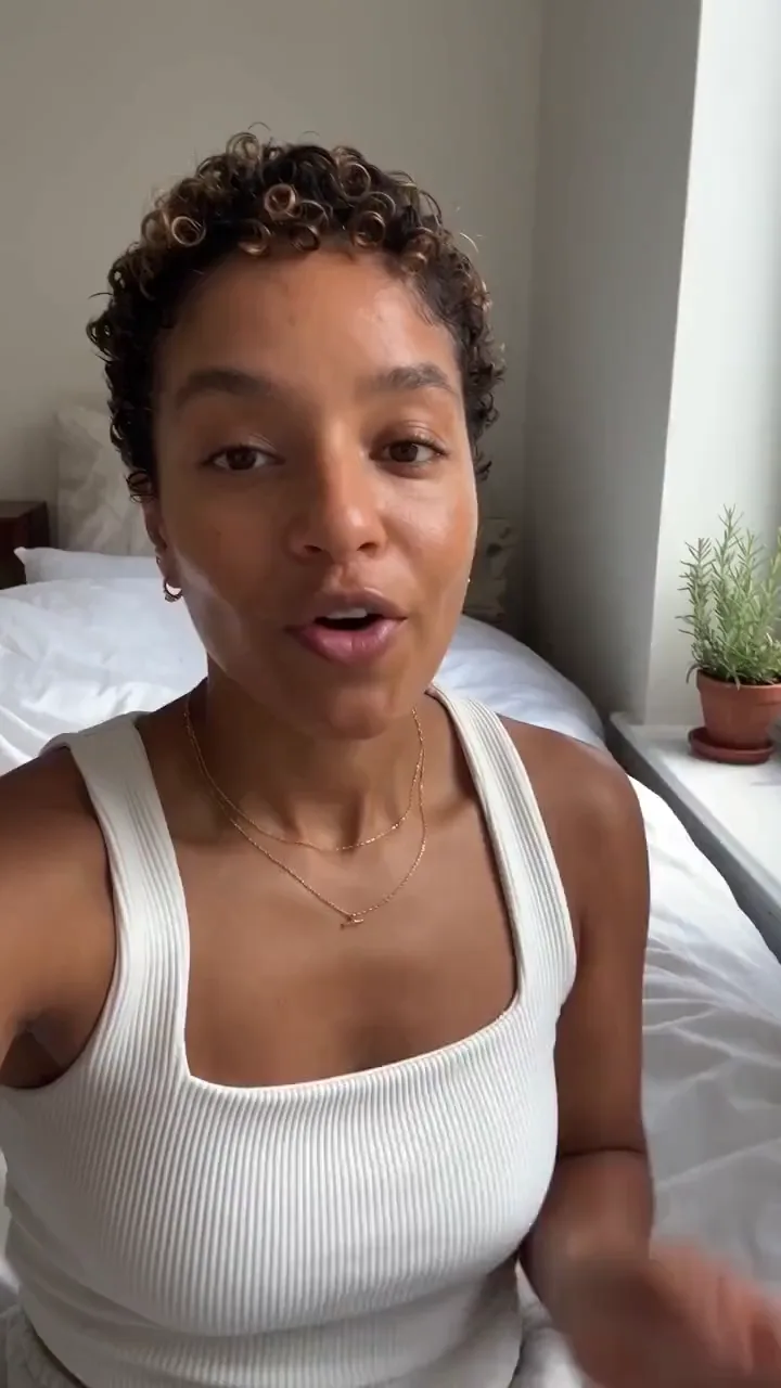 A creator on her bed talks through a tinted moisturiser and dabs it on one cheek